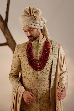 a man wearing a turban and beaded necklace stands in front of a tree