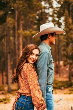 a man and woman standing next to each other in the woods