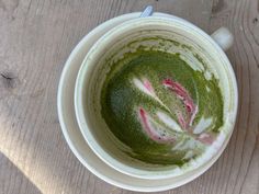 a cup filled with green and pink liquid on top of a wooden table next to a spoon