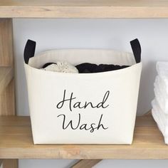 a canvas laundry basket with the words hand wash printed on it sitting on a shelf