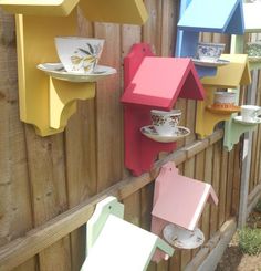 several colorful bird houses are hanging on the side of a fence with plates and cups