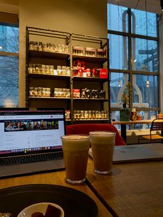 two cups of coffee sit on a table in front of a laptop computer and window