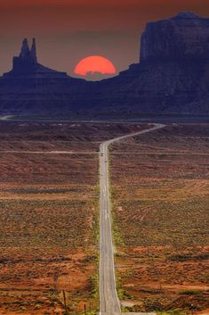 the sun is setting over an empty road in monument national park, utah with mountains in the background