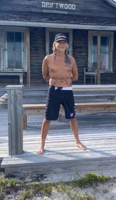 a shirtless man standing on a wooden dock in front of a building with a sign that says driftwood