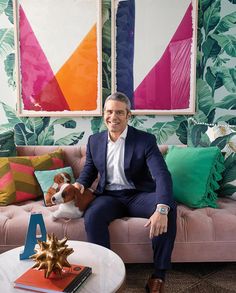 a man sitting on top of a pink couch next to a white table with a dog