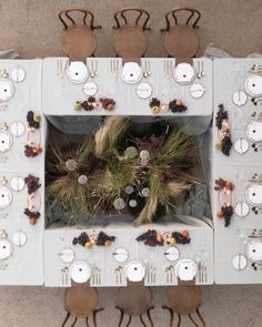 an overhead view of a table set with white plates and silverware, surrounded by brown chairs