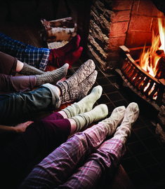 four people sitting in front of a fireplace with their feet up on the floor while wearing socks