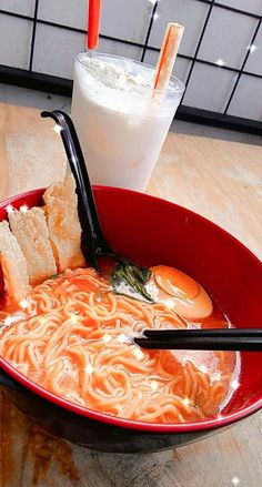 a red bowl filled with noodles and soup next to a drink