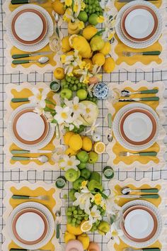 the table is set with lemons, oranges and white flowers on yellow placemats