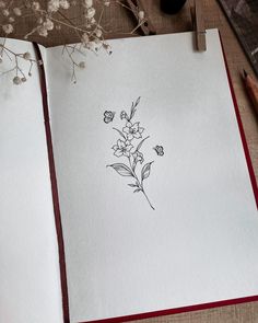 an open book with flowers drawn on it next to a pen and ink drawing supplies