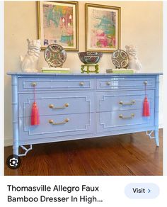 a blue dresser with gold handles and tassels on it's drawers in front of two framed pictures