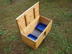 a wooden box with two blue bowls in it on the ground next to some grass