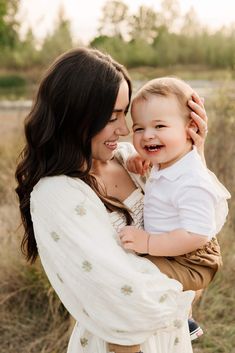 a woman holding a baby in her arms and smiling at the camera while she holds it up