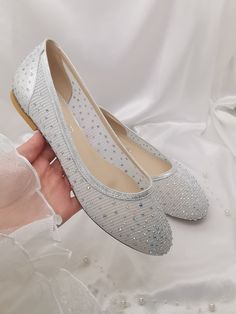 a woman's hand is holding a pair of white shoes with pearls on them