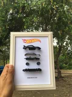 a person holding up a framed photo with four toy cars in it's shadow