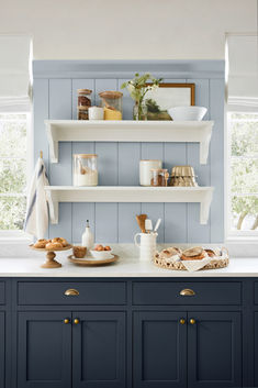 a kitchen with blue painted cabinets and white shelves filled with bread, pastries and other items