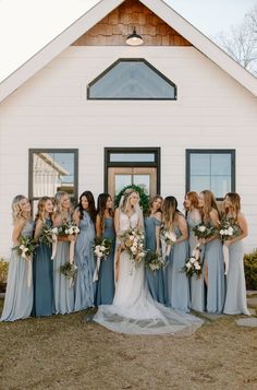 a group of bridesmaids standing in front of a white house with greenery