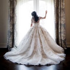 a woman standing in front of a window wearing a wedding dress and looking out the window