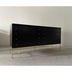 a black and gold dresser with four drawers on one side, in an empty room