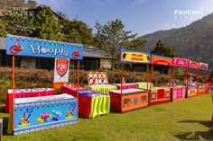 colorful booths are lined up on the grass in front of a building with mountains in the background