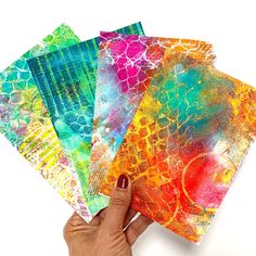 hand holding four different colored papers with designs on them, one is multicolored and the other has an abstract design