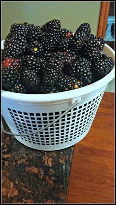 a white basket filled with blackberries sitting on top of a counter