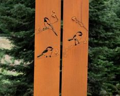 two wooden boards with birds painted on them in front of some trees and bushes,