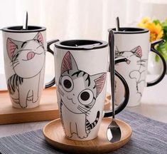 three mugs with cartoon cats on them sitting on a wooden tray next to flowers