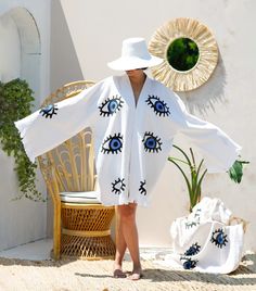 "Stay trendy and comfortable with the Evil Eye Kaftan Kimono. Made from 100% organic cotton and hand-printed with the timeless evil eye design, this Greek goddess-style kaftan is the perfect cover-up for all your summer needs.  Whether you're spending the day at the beach, picnicking in the park, or just lounging at home, the lightweight, breathable fabric will keep you cool and comfortable, and protect you from evil spirits and evil eyes. This eco-friendly and quick-drying kimono is an excellent choice for summer activities. Features *100% Cotton  *Soft, Light & Fluffy *An adjustable waist belt secures the robe from the front. Size: Length: 35.5\" - 90cm     Width: 33.5\" - 85 cm Model Height :5′ 6\"- 168 cm Care *Machine wash cold at a gentle cycle. *No bleach. *Iron on the reverse side White V-neck Kimono For Festival, White Long Sleeve Kimono For Summer, White Open Front Kimono For Festival, White Long Sleeve Summer Kimono, White Cotton Cardigan For Vacation, Handmade White Kimono For Spring, Spring White Handmade Kimono, White Long Robe For Vacation, White Robe With Kimono Sleeves For Beach Cover-up