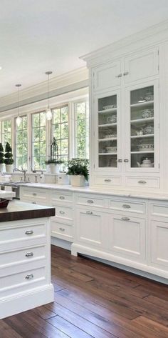 a large kitchen with white cabinets and wood flooring in the middle of it is surrounded by windows