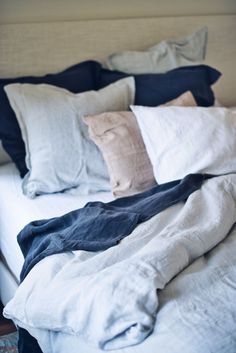 an unmade bed with many pillows and blankets