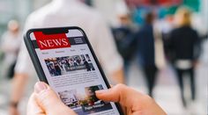 someone is holding up their cell phone to read news on the screen while walking down the street