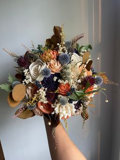 a bouquet of flowers in someones hand on a white wall behind them is an orange and purple flower arrangement