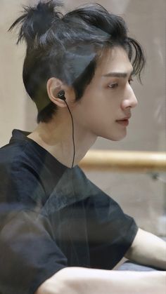 a man with ear buds on his ears sitting in front of a glass window looking at something