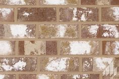 a brick wall with white and brown patches of snow on it's surface,