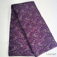 two pieces of purple fabric sitting on top of a white tablecloth covered in tiny speckles