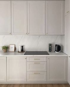 a white kitchen with marble counter tops and cupboards on the wall, along with wooden flooring