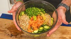 a man is holding a bowl full of vegetables and sesame seed sprouts on a wooden table