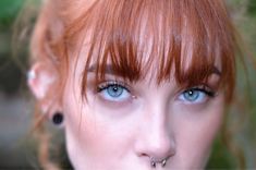 a woman with red hair and piercings on her nose is looking at the camera