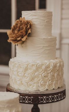 a three tiered cake with white frosting and a brown flower on the top