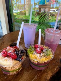 three desserts are sitting on a table next to two cups with strawberries and blueberries in them