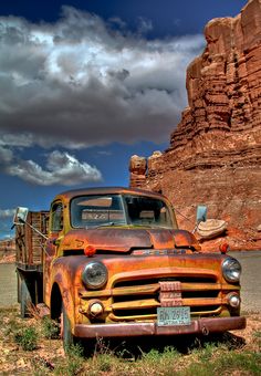 an old rusted truck parked in front of a large rock outcropping