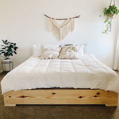 a bed with white sheets and pillows in a room next to a potted plant