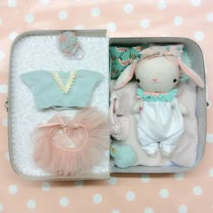 an open suitcase with two stuffed animals and other items in it on a polka dot tablecloth