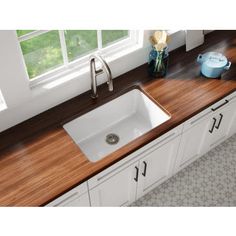 a kitchen sink sitting under a window next to a wooden counter top in front of a window