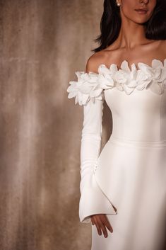 a woman in a white dress with flowers on her shoulder and arms, posing for the camera