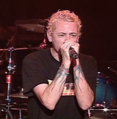 a man holding a microphone up to his mouth while standing in front of a drum set