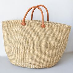 Sisal is a flowering plant that has been cultivated and naturalized in Kenya and the strong fibers that come from it are used to make various items from rope to bags. These durable baskets can handle a heavy load without breaking a sweat while looking handsome at the same time! Woven from natural sisal plant fibers with leather handles. A Kenyan market artisan partnership. Learn more about our artisans' handmade products here. Details: 14" T 20.5" W Colors and designs vary due to the handmade na Natural Fiber Bucket Bag With Handles, Beige Basket Bucket Bag With Rolled Handles, Natural Bucket Bag With Braided Handles For Market, Natural Crochet Jute Bag With Rolled Handles, Beige Basket Beach Bag With Rolled Handles, Natural Straw Basket Bag With Rolled Handles, Natural Basket Beach Bag With Rolled Handles, Everyday Neutral Handwoven Straw Bag, Beige Bucket Straw Bag For Market