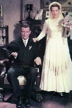 an old photo of a man and woman dressed in formal wear sitting on a chair