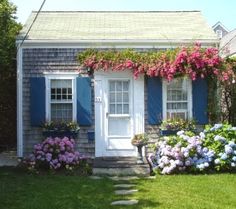 a house with blue shutters and flowers in the front yard